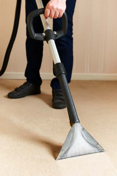 This is a photo of a man steam cleaning a cream carpet, using a professional steam cleaning machine works carried out by Penge Carpet Cleaning