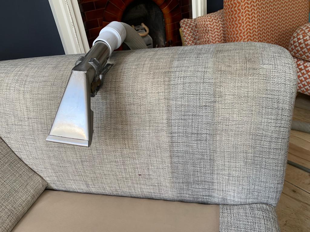 This is a photo of Penge Carpet Cleaning arm of beige sofa that shows a test patch that has been steam cleaned. The steam cleaning machine is also showing in the photo.